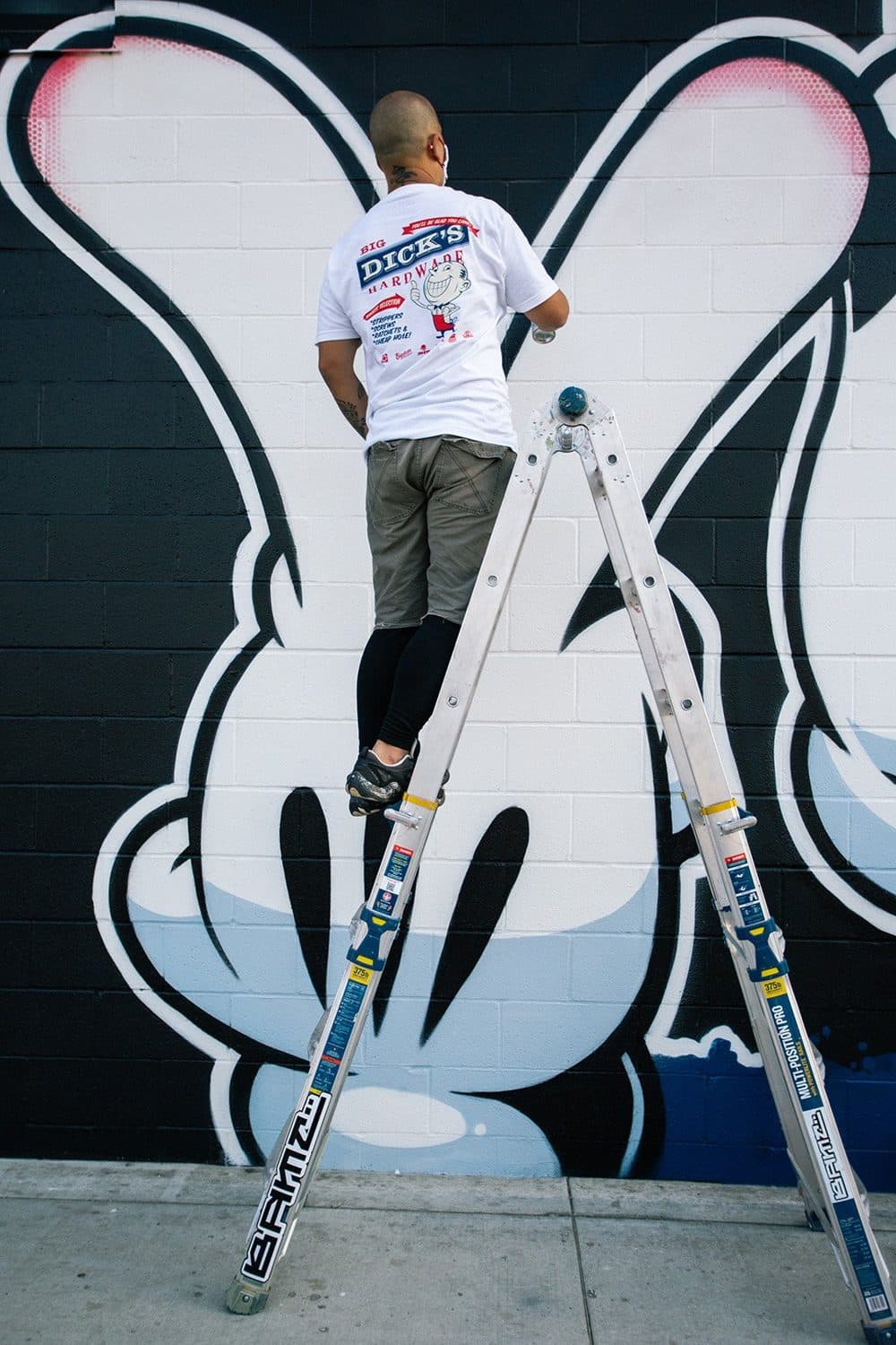 Slick paints the glove-hand letterforms from a ladder.